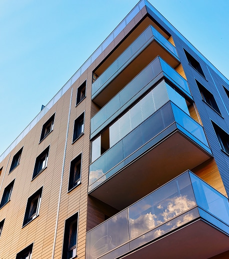 Immeuble moderne : Balcons d'angle en verre et design de façade. Immeuble d'appartements moderne. Façades beige et gris, balcons d'angle en verre contemporains. Reflets des nuages dans les garde-corps.