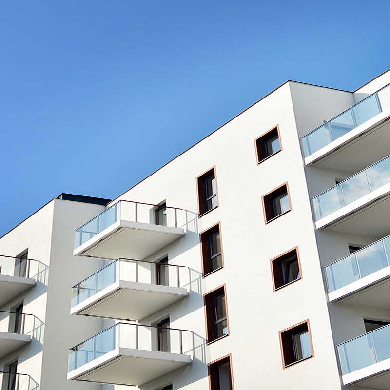 Architecture moderne: Immeuble blanc épuré et balcons verre. Immeuble résidentiel moderne. Façade blanche épurée, soulignée par des balcons en porte-à-faux avec garde-corps en verre sous un ciel bleu.