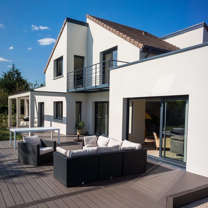 Terrasse deck composite & Salon de jardin de maison moderne. Maison contemporaine blanche, terrasse en deck composite foncé. Salon de jardin noir, baies vitrées et balcon métallique.
