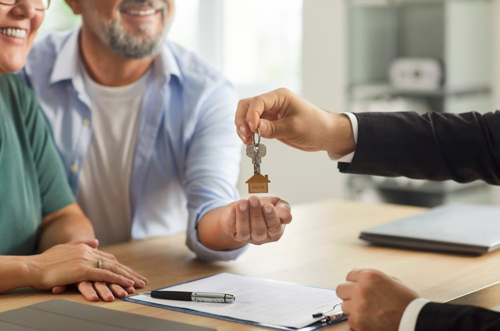 Remise des clés : couple heureux pour leur achat immobilier. Remise des clés "Home" à un couple heureux par un agent immobilier en costume. Le contrat d'achat est sur la table.